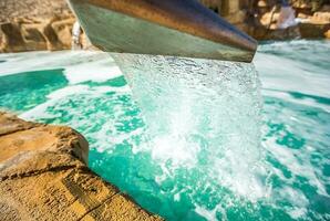 Stream water out of artificial waterfall in outdoor pool photo