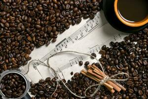 Coffee beans, cinnamon sticks and cup of brewed coffee on sheet music background, view from above with space for text photo