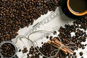 Coffee beans, cinnamon sticks and cup of brewed coffee on sheet music background, view from above with space for text photo