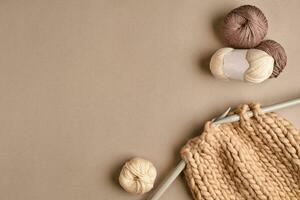 White and brown knitting wool and knitting on knitting needles on beige background. Top view. Copy space photo