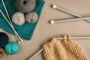 Grey and turquoise knitting wool and knitting on knitting needles on beige background. Top view. Copy space photo