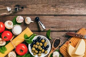 Raw ingredients for the preparation of Italian pasta, spaghetti, basil, tomatoes, olives and olive oil on wooden background. Top view. Copy space. photo