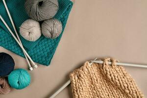 Grey and turquoise knitting wool and knitting on knitting needles on beige background. Top view. Copy space photo