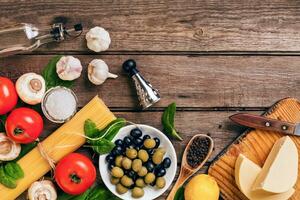 Raw ingredients for the preparation of Italian pasta, spaghetti, basil, tomatoes, olives and olive oil on wooden background. Top view. Copy space. photo