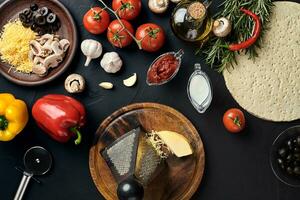 Cheese, different vegetables on black table. Ingredients for traditional italian pizza. photo