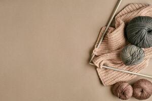 Grey and brown knitting wool and knitting on knitting needles on beige background. Top view. Copy space photo