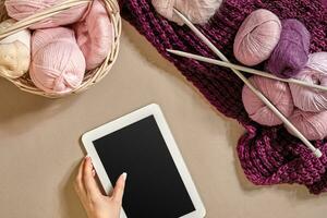 Pink and purple balls of wool threads with knitting needles lying in basket on beige background. Mock up background for your craft knitting photo