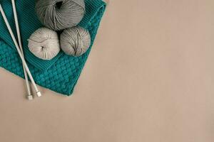 Grey and turquoise knitting wool and knitting needles on beige background. Top view. Copy space photo