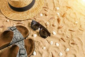 Summer beachwear, flip flops, hat, sunglasses and seashells on sand beach. photo