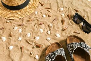 Summer beachwear, flip flops, hat, sunglasses and seashells on sand beach. photo