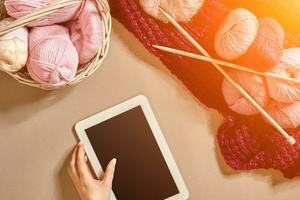 Pink and purple balls of wool threads with knitting needles lying in basket on beige background. Mock up background for your craft knitting. Sun flare photo