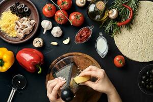 Female hands rubbed cheese grated on pizza, ingredients for cooking pizza on black table, top view photo