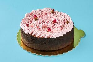 Delicious pink cream cake decorated with a small dried rosebuds, standing on a gold stand against a blue studio background. photo