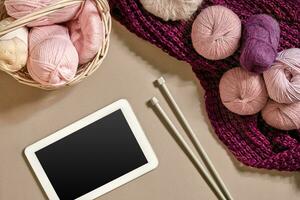 Pink and purple balls of wool threads with knitting needles lying in basket on beige background. Mock up background for your craft knitting photo