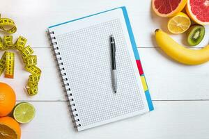 Fresh fruits with tape measure over white wooden background. Top view photo