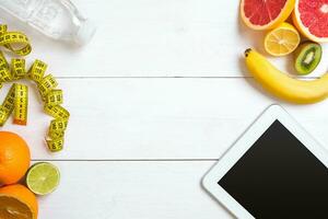 Healthy breakfast with oatmeal, fresh fruits and bottle of water with tablet on rustic wooden table. photo