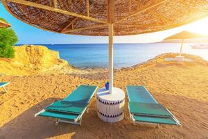 Umbrella and two empty deckchairs on the shore sand beach photo