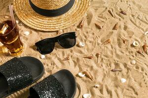 Summer beachwear, flip flops, hat, cold drink in a glass and seashells on sand beach. photo