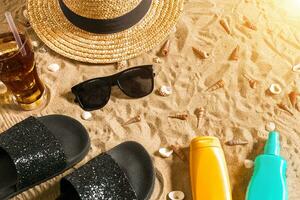 Summer beachwear, flip flops, hat, cold drink in a glass and seashells on sand beach. photo