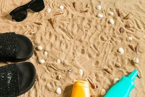 Black flip-flops and sunglass, seashell on sand. With place for your text. Top view photo