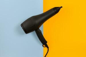 Black hair dryer on blue and yellow paper background photo