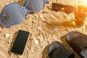 Summer bikini and accessories stylish beach set, Beach bikini summer outfit and sea sand as background, Top View, Concept photo