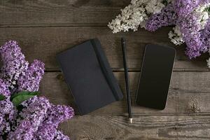 Lilac blossom on rustic wooden background with notebook for greeting message. Top view photo