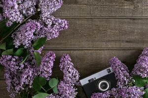 Lilac blossom on rustic wooden background with empty space for greeting message. Camera old. Top view photo