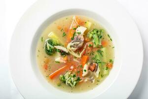 Light fish soup with vegetables and broccoli in white plate. photo