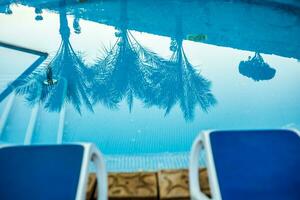 Closeup sunloungers and swimming pool with reflected palms in water photo