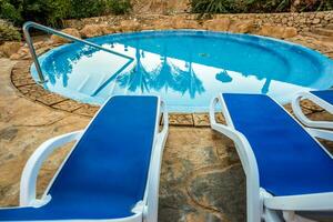 tumbonas y nadando piscina con reflejado palmas en agua foto