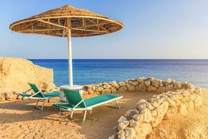 Umbrellas and two empty deckchairs on the shore sand beach photo