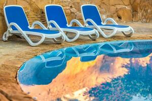 Three sunloungers reflected in blue water of the swimming pool photo