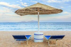 Umbrella and two empty deckchairs on the shore sand beach photo