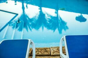 Closeup sunloungers and swimming pool with reflected palms in water photo