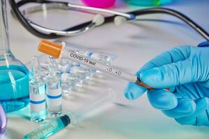 Hands in gloves holding Coronavirus testing kit. Medical flasks, colorful chemical reagents. Ampoules, syringe, phonendoscope isolated on white photo