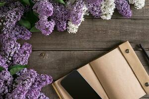 Lilac blossom on rustic wooden background with notebook for greeting message. Top view photo