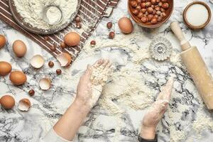 de cerca disparo. parte superior ver de un panadero cocinar lugar, manos son trabajando con un crudo masa en el mármol mesa antecedentes. foto