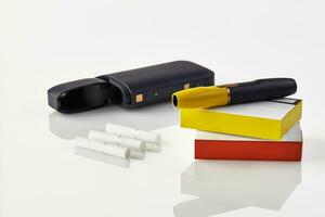 Black electronic cigarette is on packs with red and yellow sides, open battery, three heatsticks isolated on white. Heating tobacco system. Close up photo