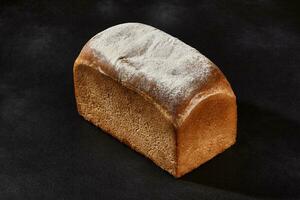 Whole loaf of fresh, delicious baked white bread sprinkled with flour. Black background with copy space. Close-up photo