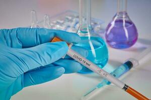 Hands in blue gloves holding testing kit. Medical flasks, colorful chemical reagents. Ampoules and syringe isolated on white. Coronavirus. Close up photo