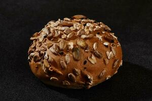 Fresh, delicious baked bun with seeds and oat flakes against black background with copy space. Rural cuisine or bakery. Close-up photo