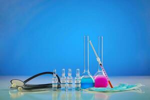 Medical flasks with colorful chemical reagents. Six ampoules with liquid, testing kit, mask and phonendoscope, blue background. Coronavirus , pandemic photo