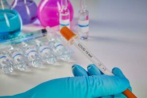 Hand in blue glove holding testing kit. Medical flasks, colorful chemical reagents. Ampoules and syringe isolated on white. Coronavirus. Close up photo