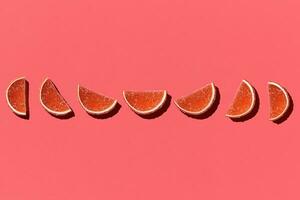 Pattern made of colorful candied fruits orange lemon on coral background. Flat lay. Minimal concept photo