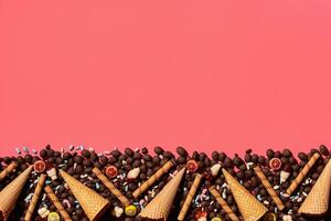 Chocolate dragee and waffle cones placed in fascinating order on coral background, view from above photo