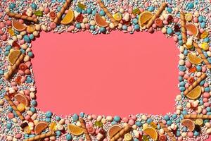 Multicolored glazed dragees and other sweets are arranged in the form of a frame on a coral background. photo