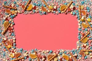 Multicolored glazed dragees and other sweets are arranged in the form of a frame on a coral background. photo