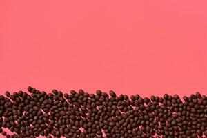 Chocolate dragee are placed in fascinating order on coral background, view from above photo
