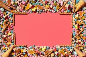 Multicolored glazed dragees and other sweets are arranged in the form of a frame on a coral background. photo